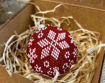 Op de afbeelding: Een rood-witte, met kralen bezette kerstbal met een sneeuwvlokpatroon, gepresenteerd in een kartonnen doos met stro. De bal heeft een diameter van ongeveer 7.6 cm, perfect voor feestelijke decoraties.