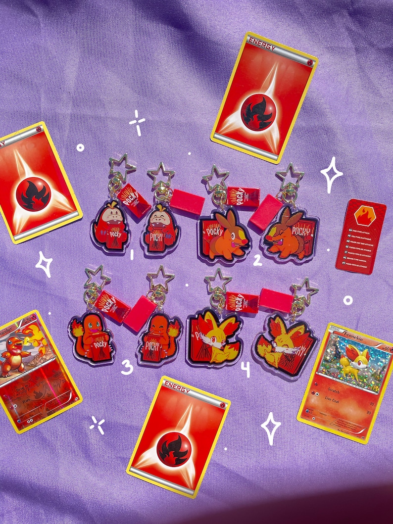 May include: Six clear acrylic keychains featuring Pokemon characters from the Fire type. Each keychain has a red and white Pocky snack wrapper design. The keychains are arranged in two rows of three. The keychains are on a purple background with red and white energy cards and a Fennekin card.