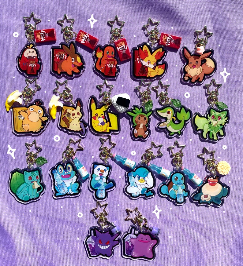 May include: A collection of 18 colorful acrylic charms featuring Pokemon characters. The charms are attached to gold keychains and feature various Pokemon, including Pikachu, Bulbasaur, Squirtle, Charmander, Eevee, and more. The charms are displayed on a purple background.