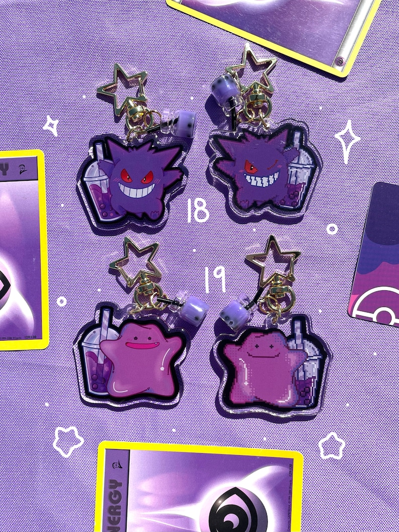 May include: Four purple and white Pokemon character charms with boba tea. The charms are attached to gold chains with star-shaped charms. The characters are Gengar and Jigglypuff.