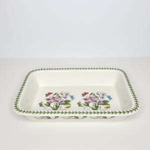 May include: A rectangular cream-colored ceramic baking dish featuring a green leaf border pattern. The interior base displays two floral illustrations of pink and purple sweet pea flowers with small butterflies, labeled with the text Lathyrus.