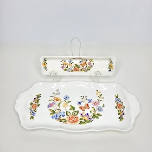 May include: A white ceramic rectangular serving tray and a matching long narrow rectangular dish, both featuring scalloped edges and a colorful floral pattern with butterflies in shades of orange, blue, yellow, pink, and green on a white background.