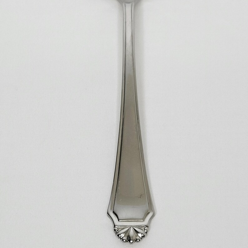 May include: A stainless steel fork with a decorative floral design at the base of the handle. The fork has a polished, reflective surface and a simple, elegant design, suitable for formal dining.