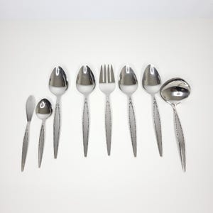 May include: A set of eight stainless steel flatware pieces including a small spreader, a small spoon, two large spoons, a four-tined fork, two additional large spoons, and a ladle. Each piece features a tapered handle with a textured border.