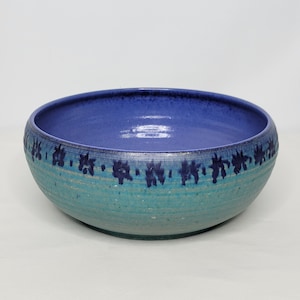May include: A large, blue and green ceramic bowl with a decorative pattern of blue flowers around the rim.