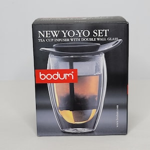 May include: A black box with the text "NEW YO-YO SET" and "TEA CUP INFUSER WITH DOUBLE WALL GLASS". The box features a clear double-walled glass tea cup with a black infuser and the Bodum logo.
