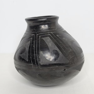 May include: Black pottery vase with geometric designs. The vase is round and has a wide mouth.