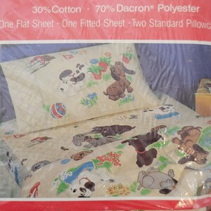 Pode incluir: Um conjunto de len&ccedil;&oacute;is com um desenho de c&atilde;o de desenho animado com o texto "Pound Puppies Lovable, Huggable". O conjunto inclui um len&ccedil;ol de cama, um len&ccedil;ol de el&aacute;stico e duas fronhas padr&atilde;o. O tecido &eacute; uma mistura de 30% algod&atilde;o e 70% poli&eacute;ster Dacron.