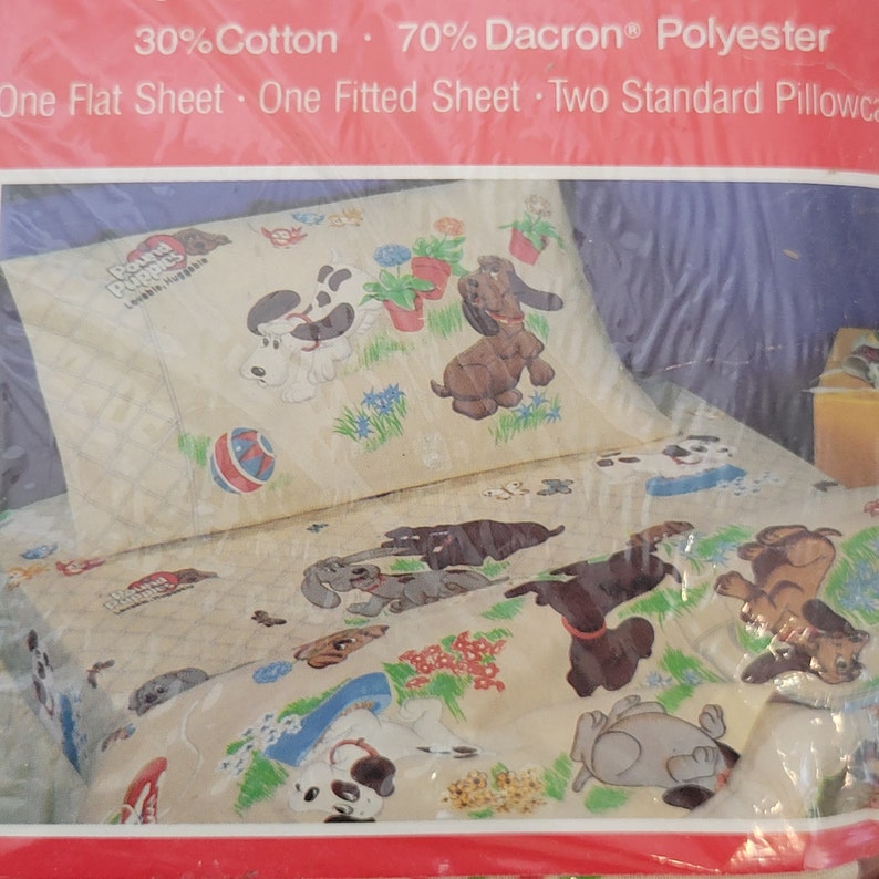 Pode incluir: Um conjunto de len&ccedil;&oacute;is com um desenho de c&atilde;o de desenho animado com o texto "Pound Puppies Lovable, Huggable". O conjunto inclui um len&ccedil;ol de cama, um len&ccedil;ol de el&aacute;stico e duas fronhas padr&atilde;o. O tecido &eacute; uma mistura de 30% algod&atilde;o e 70% poli&eacute;ster Dacron.