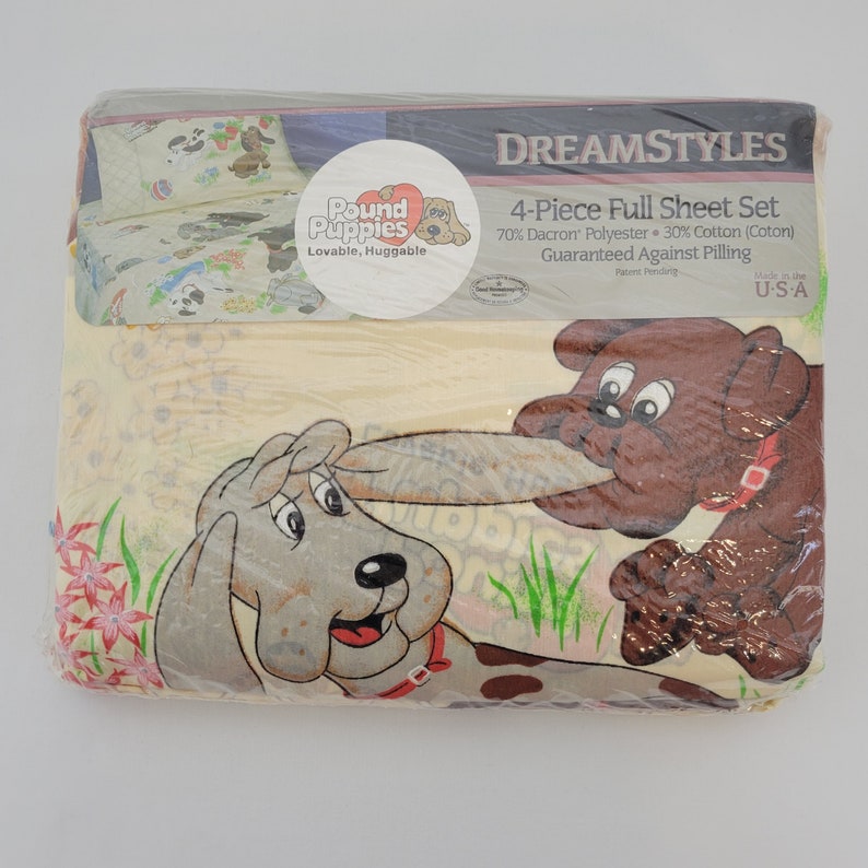 Pode incluir: Uma embalagem para um conjunto de len&ccedil;&oacute;is completos de 4 pe&ccedil;as com um design de c&atilde;o de desenho animado. A embalagem &eacute; amarela com c&atilde;es marrons e cinzentos. O texto na embalagem diz "Pound Puppies Lovable, Huggable" e "DREAMSTYLES 4-Piece Full Sheet Set 70% Dacron Polyester 30% Cotton (Coton) Guaranteed Against Pilling Made in the U-S-A".
