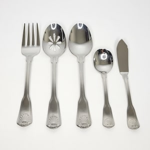 May include: A set of five stainless steel utensils featuring a polished finish and a decorative shell motif at the base of each handle. The set includes a four-tined fork, a slotted spoon, a solid spoon, a small spoon, and a flat-edged butter knife.