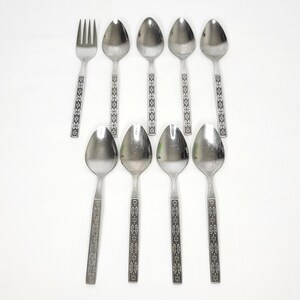 May include: A collection of stainless steel silverware, including spoons and a fork, arranged on a white surface. The silverware features a decorative floral pattern on the handles. The spoons have an oval bowl shape.