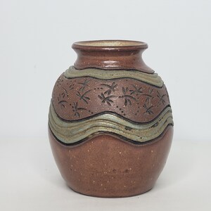 May include: A small, brown ceramic vase with a wavy, light blue and brown design. The vase is decorated with a pattern of small, carved leaves.