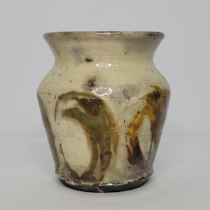 May include: A small, white ceramic vase with brown and green glaze. The vase has a rounded body and a slightly flared opening.
