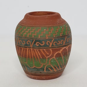 May include: A small, terracotta pot with green and brown geometric designs. The pot is decorated with a repeating pattern of waves and stylized flowers.