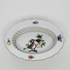 May include: White oval porcelain dish with a woven basket design. The center features a hand-painted scene of two birds perched on a branch with green leaves and white berries. The rim is decorated with a gold trim and four hand-painted insects.