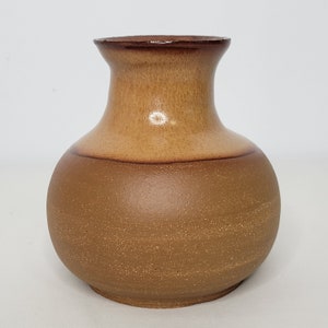May include: A brown ceramic vase with a rounded body and a slightly flared opening. The vase has a light brown glaze on the top half and a darker brown glaze on the bottom half.
