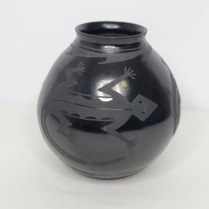 May include: Black pottery vase with a lizard design. The vase is round and has a smooth, glossy finish.
