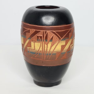 May include: A small, black and brown ceramic vase with a geometric design. The vase is decorated with a band of brown, yellow, and blue geometric patterns.