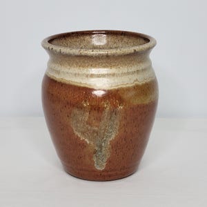 May include: A brown ceramic vase with a white rim and a speckled glaze. The vase has a rounded body and a wide opening.