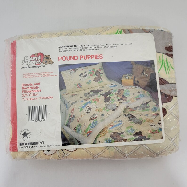 Pode incluir: Uma embalagem para len&ccedil;&oacute;is e fronhas revers&iacute;veis Pound Puppies. A embalagem &eacute; amarela com uma ilustra&ccedil;&atilde;o de um c&atilde;o de ca&ccedil;a marrom e branco. O texto na embalagem diz "Pound Puppies Lovable, Huggable" e "Len&ccedil;&oacute;is e fronhas revers&iacute;veis 30% algod&atilde;o 70% poli&eacute;ster Dacron".