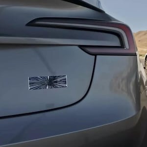 May include: A gray Tesla Model 3 with a black and white Star Wars Death Star sticker on the back bumper.