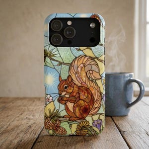Könnte beinhalten: Eine Smartphone-Hülle mit einem Design im Buntglas-Stil, das ein braunes Eichhörnchen mit einer Eichel zeigt. Der Hintergrund umfasst hellblauen Himmel, Sonnenstrahlen, Tannenzapfen und violette Blumen. Die Hülle hat einen schwarzen Kameraausschnitt.
