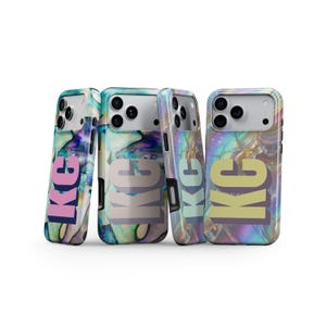 Puede incluir: Cuatro fundas para teléfono con un patrón de mármol arremolinado, iridiscente y multicolor en tonos azules, morados y verdes. Cada funda muestra el texto en letras mayúsculas "KC" en varios colores, incluyendo rosa, gris claro, azul claro y amarillo.