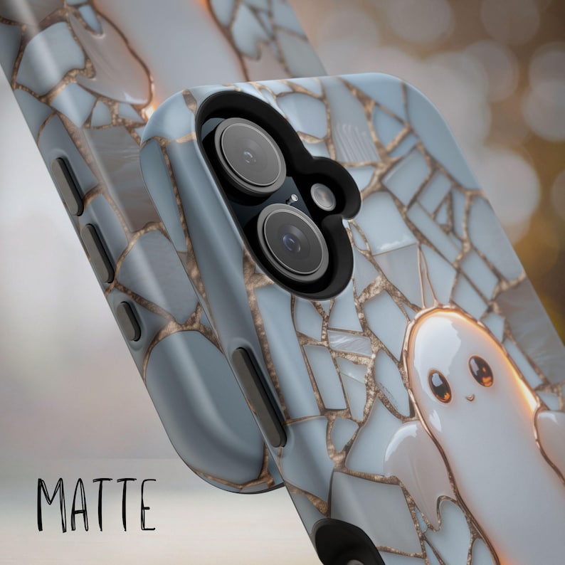 May include: A phone case featuring a light blue and white mosaic pattern with gold-colored grout lines. A small, white, cartoon-style ghost with large eyes is visible on the back. The case has a black camera cutout and the word MATTE printed below.