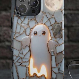 May include: A smartphone case featuring a white ghost character with large dark eyes centered on a background of white and gold mosaic tiles. A full moon is visible in the upper right corner. The case has a cutout for a triple camera system.