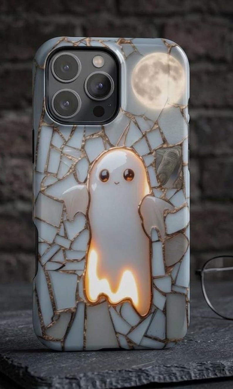May include: A smartphone case featuring a white ghost character with large dark eyes centered on a background of white and gold mosaic tiles. A full moon is visible in the upper right corner. The case has a cutout for a triple camera system.