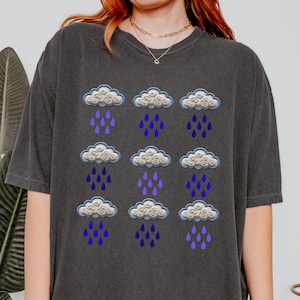 May include: A dark gray t-shirt with a repeating pattern of white clouds with purple raindrops.