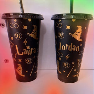 May include: Two black reusable cups with gold accents and a Harry Potter theme. The cups have the numbers "9 3/4" and a lightning bolt. One cup says "Laura" and the other says "Jordan".