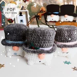 May include: Crocheted snowman figures with top hats in various colors. The snowmen have carrot noses and button eyes. The image includes the text "PDF PATTERN". Decorative snowflakes are scattered around the snowmen.