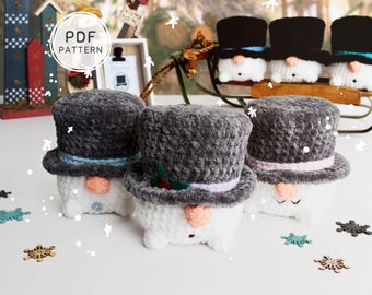 May include: Crocheted snowman figures with top hats in various colors. The snowmen have carrot noses and button eyes. The image includes the text "PDF PATTERN". Decorative snowflakes are scattered around the snowmen.