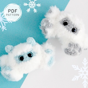 May include: Two plush, white and gray toy creatures with large black eyes and blue accents. The toys are shaped like small animals and are set against a light blue and white background with snowflake decorations. The image includes the text "PDF PATTERN".