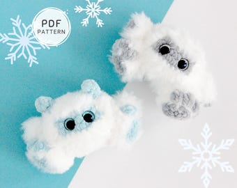 May include: Two plush, white and gray toy creatures with large black eyes and blue accents. The toys are shaped like small animals and are set against a light blue and white background with snowflake decorations. The image includes the text "PDF PATTERN".