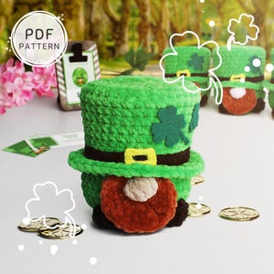 May include: A green crocheted leprechaun hat with a shamrock on the front. The hat is sitting on a table with gold coins scattered around it. The hat is part of a set of crocheted leprechaun hats.