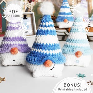 May include: A collection of handmade crochet gnomes with white bodies and colorful striped hats in blue, purple, and light blue. Each gnome has an orange nose and a small button. The image includes the text "PDF PATTERN" and "BONUS! Printables Included".