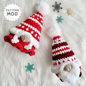 May include: Two handmade crochet gnome hats in red and white stripes with white trim and a fluffy white pom-pom. The hats have a tan nose and a white beard. The image includes the text "PATTERN MOD".