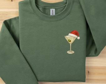 Può includere: Felpa verde con un design ricamato festivo. Il design presenta un bicchiere da martini con un'oliva e un cappello da Babbo Natale. La felpa è realizzata in un materiale morbido, ideale per le festività.