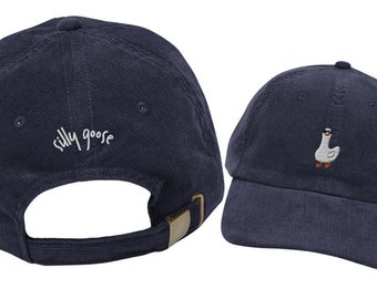 May include: A navy blue corduroy baseball cap with the text "silly goose" embroidered on the front. The back of the cap features a white goose with sunglasses embroidered on it.
