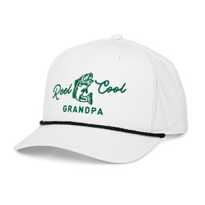 May include: White baseball cap with a black rope detail and a curved brim. The cap features the text "Reel Cool Grandpa" in green script and a graphic of a fish.
