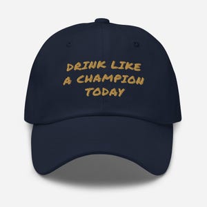 May include: A navy blue baseball cap with the text "Drink Like A Champion Today" embroidered in gold.
