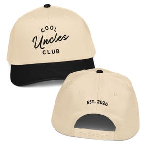 May include: A beige and black baseball cap with the text "COOL Uncles CLUB" in black script on the front. The back of the cap has the text "EST. 2026". The cap has a black brim and a black button on top.