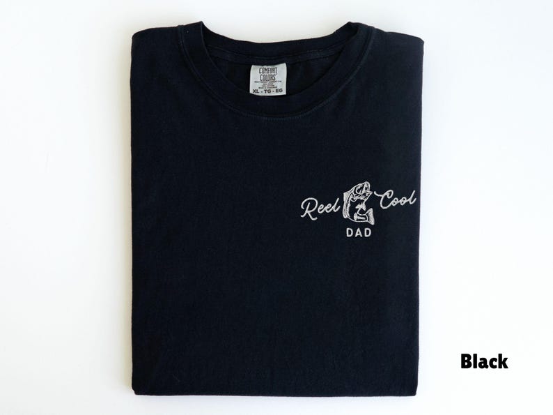 Pu&ograve; includere: T-shirt nero con la scritta "Reel Cool Dad" in bianco. La maglietta ha una piccola grafica di un pesce. La maglietta &egrave; piegata e ha un'etichetta in alto al centro.