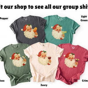 May include: A collection of five t-shirts in various colors: pepper, light green, moss, ivory, and crimson. Each shirt features a Santa Claus graphic with a cocktail or wine glass. The text "Visit our shop to see all our group shirts!" is at the top.