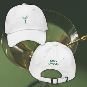 May include: White baseball cap with a green embroidered martini glass on the front. The back of the cap features the text "Kate's Dirty 30" in green. The cap has an adjustable strap.