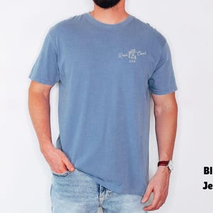Pu&ograve; includere: Una maglietta blu a maniche corte con la scritta "Reel Cool Dad" in bianco. La maglietta &egrave; abbinata a jeans blu. L'aspetto generale &egrave; casual e confortevole.
