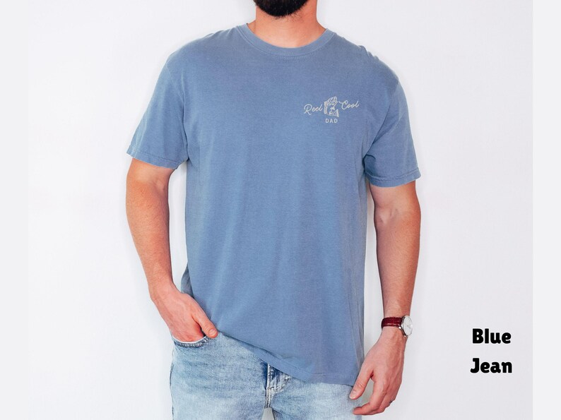 Pu&ograve; includere: Una maglietta blu a maniche corte con la scritta "Reel Cool Dad" in bianco. La maglietta &egrave; abbinata a jeans blu. L'aspetto generale &egrave; casual e confortevole.